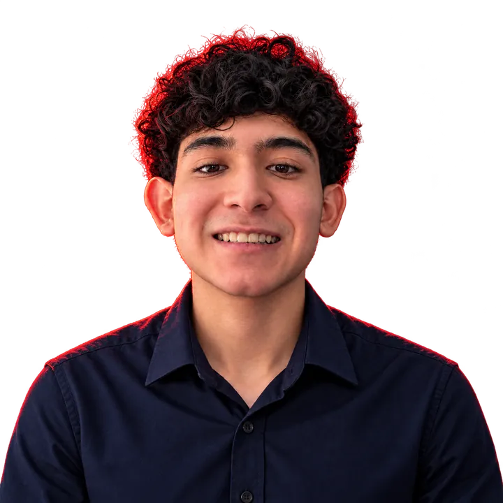 Retrato de Jesús David Gómez Torregroza, sonriente, con camisa oscura y luz roja de contorno sobre el cabello rizado.